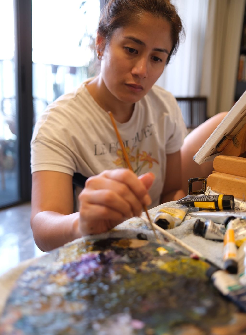 Sap mixing paint on her palette, brush in hand, beside a canvas on her easel