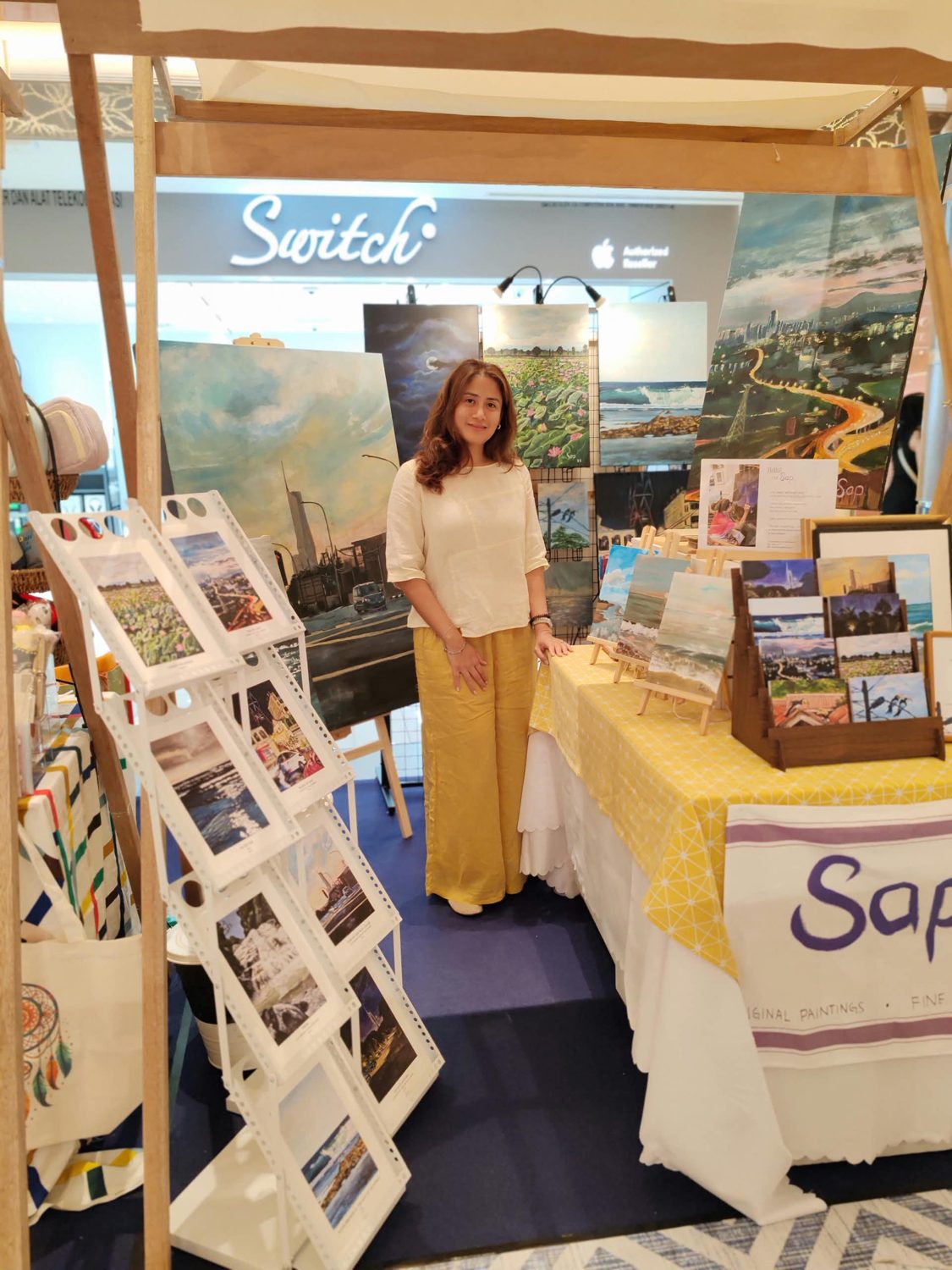 Sap at her booth at the Seek & Keep Artisan Market, surrounded by her paintings and prints